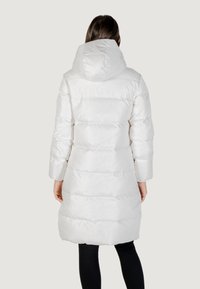 Cappotto bianco, morbido, lungo fino al ginocchio con cappuccio, caratterizzato da un design trapuntato e una texture liscia. Maniche lunghe e vestibilità comoda.