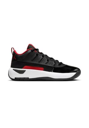 Zapatilla deportiva baja en negro y rojo con parte superior perforada, entresuela blanca, suela exterior negra y forro interior rojo, mostrada de perfil.