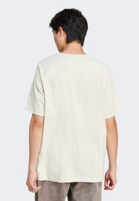 T-shirt court à manches courtes beige clair avec col rond et manches raglan, fabriqué en coton doux, présentant une texture lisse et une coupe décontractée.