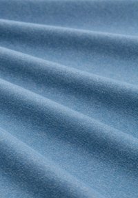 Tissu en denim bleu avec une texture lisse, présentant des variations subtiles de couleur et un motif de sergé régulier, plié en ondulations.