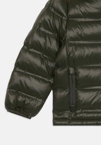 Mørkegrøn pufferjakke med en blank finish, vandret quiltet design, elastiske manchetter og en lynlåslomme på venstre side.