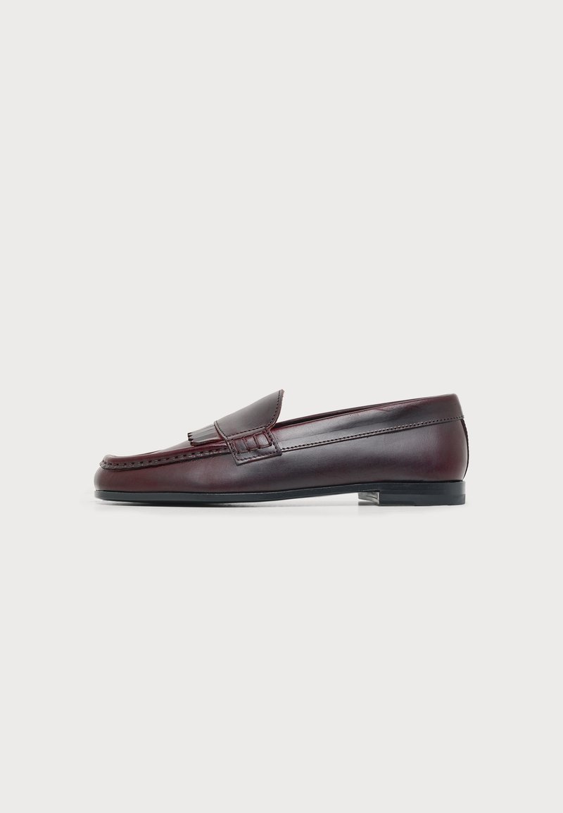 Mocassin classique en cuir marron foncé avec détail pompon et petit talon noir, vu de côté sur fond blanc.