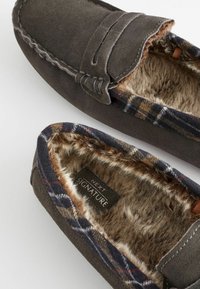 Donkergrijze suède sloffen met een platte design, voorzien van een geruite voering, zachte bontinterieur en decoratieve stiksels op de bovenkant.