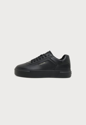 Baskets basses en cuir noir avec lacets noirs et logo Calvin Klein sur le côté, présentées de côté sur fond blanc.