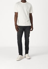 Světlé béžové tričko s kulatým výstřihem v kombinaci s tmavě modrými džínami a bílými teniskami. Bavlněná látka, přiléhavý střih, jednoduché detaily bez vzorů.