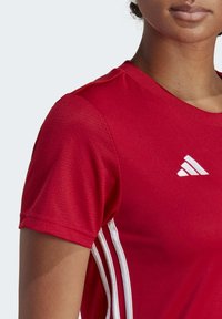 Rode sportieve t-shirt met korte mouwen, gemaakt van ademend materiaal; heeft witte accentstrepen en een logo op de borst.