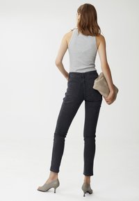 Jeans negros de talle alto con una textura suave y diseño ajustado, combinados con una camiseta sin mangas gris y un bolso de mano beige. Zapatos de tacón en tono piel.