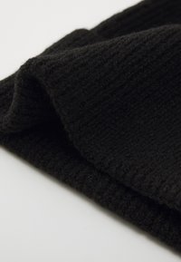 Black knitted fabric with a textured, ribbed pattern, shown in a folded position to highlight its softness and thickness.