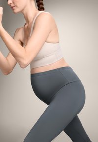 Svetlo bež športni modrček v kombinaciji s temno sivo športnimi leginami, oboje narejeno iz raztegljive tkanine, zasnovano za udobje med gibanjem.