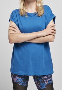 T-shirt blu a maniche corte con orli arrotolati, realizzato in morbido cotone. Abbinato a leggings neri con un motivo pixelato blu e rosa.