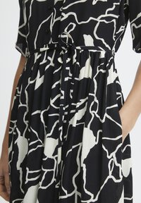 Vestido de rayas en blanco y negro con un corte relajado, mangas cortas, botones en el cuello y un detalle de lazo en la cintura. Tejido texturizado, falda acampanada.