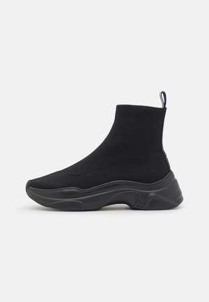 Basket montante noire style chaussette avec bord-côte à la cheville, languette à la talonnette et semelle épaisse en caoutchouc sculptée, montrée de profil sur fond blanc.