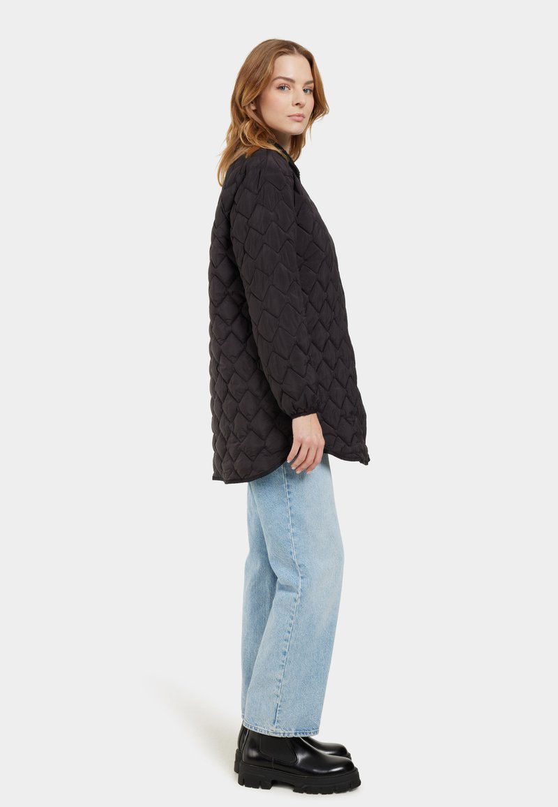 Schwarze gesteppte Jacke mit lockerer Passform und strukturiertem Muster. Kombiniert mit hellblauen Jeans mit geradem Bein und schwarzen Stiefeletten.