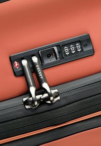 Valigia arancione con una serratura di sicurezza nera, cerniere in metallo e un pannello con combinazione. La finitura testurizzata migliora la presa e la durata.