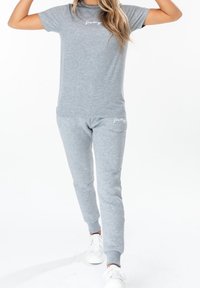 Grijze katoenen t-shirt met korte mouwen en een ronde halslijn, gecombineerd met bijpassende grijze joggingsbroeken met een logo op de heup. Witte sneakers.