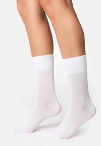 Chaussettes blanches à chevilles en tissu fin et respirant avec un bord côtelé. Texture lisse, design minimaliste, sans motifs ni logos visibles.