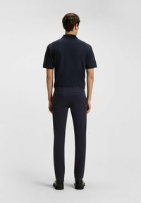 Camisa de polo azul marino con cuello y mangas cortas, combinada con pantalones oscuros ajustados y zapatos negros, vista desde la parte posterior. Diseño simple y moderno.