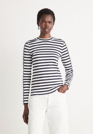 Langarm gestreept shirt in marineblauw en witte katoen, met een ronde hals en ingewikkelde details langs de mouwen, gestyled met witte broek.