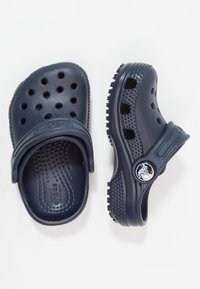 Zoccoli Crocs blu navy realizzati in materiale sintetico, con fori di ventilazione, una cinghia e suole testurizzate per grip e comfort.
