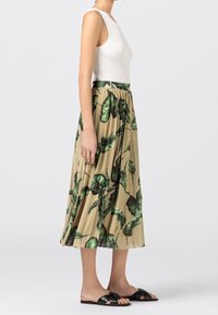 Beige plisserad kjol med grön bladmönster, i kombination med en vit ribbad linne och svarta sandaler, som visar en avslappnad passform och flödande design.