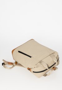Zaino beige con un'esterno testurizzato, dettagli in pelle marrone a contrasto, spallacci regolabili e chiusura superiore con zip e tasche laterali.