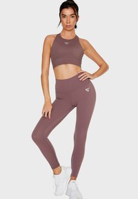 Sostenitore sportivo e leggings a vita alta in un colore mauve smorzato, realizzati in tessuto elastico. Logo distintivo sulla gamba e linee di design eleganti.