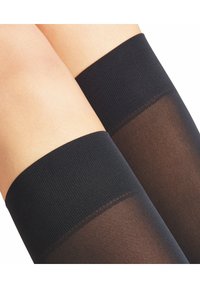 Czarne nagolenniki do ud z prążkowanym elastycznym paskiem na górze i przezroczystym materiałem. Teksturowany górny brzeg zapewnia stabilne dopasowanie.