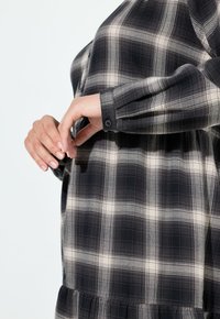 Czarna i biała koszula w kratę z długim rękawem, zapięciem na guziki przy mankietach oraz marszczonym dołem, wykonana z miękkiego, teksturowanego materiału z wyraźnym wzorem kratki.
