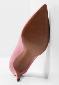 Chaussure à talon haut en daim rose avec un bout pointu et un talon stiletto fin. La semelle est marron, avec un branding minimal.