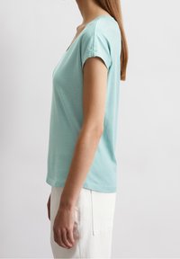 Ljusblå bomulls-t-shirt med avslappnad passform, korta ärmar och en blygsam V-hals. Kombineras med vita byxor för en avslappnad stil.