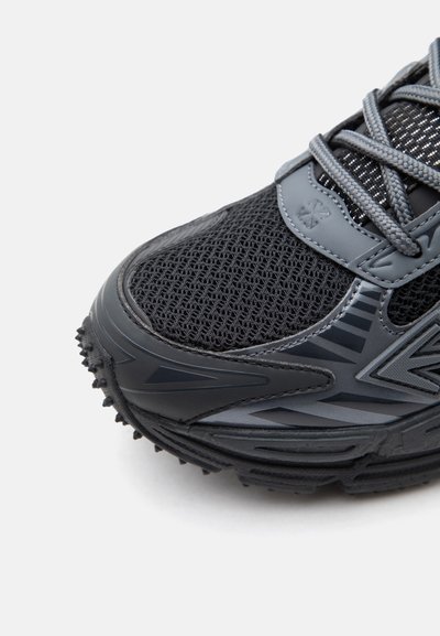 Κοντινό πλάνο αθλητικού παπουτσιού σε μαύρο και γκρι με επάνω μέρος από δίχτυ, υφασμένο καουτσούκ στη σόλα και γκρι κορδόνια σε λευκό φόντο.