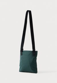 Zöld szövet válltáska fekete pánttal, téglalap alakú, felső cipzáras záródással, megerősített sarkokkal és sima textúrával.