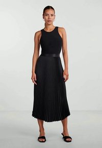Vestido preto sem mangas com um corpete ajustado e uma saia plissada, apresentando uma textura suave e uma silhueta fluida.