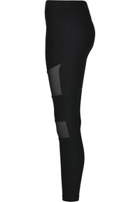 Leggings noirs à côtes avec des panneaux en mesh sur les côtés. Le design comprend une taille haute et une silhouette ajustée.