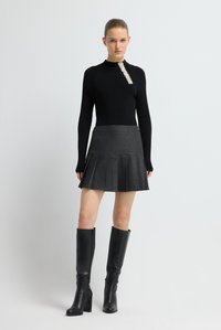 Zwarte ribgebreide trui met een gestructureerde versiering bij de halslijn, gecombineerd met een geplooide grijze rok en kniehoge zwarte leren laarzen.