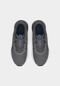 Ζευγάρι γκρι αθλητικά παπούτσια Puma με μπλε λογότυπο, λευκές ενδιάμεσες σόλες και γκρι κορδόνια, φωτογραφημένα από πάνω σε λευκό φόντο.