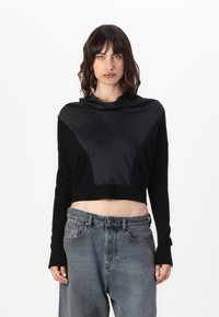 Maglione nero cropped con un pannello frontale in satin a contrasto, maniche lunghe e un collo alto, abbinato a pantaloni in denim grigi sbiaditi a vita alta.