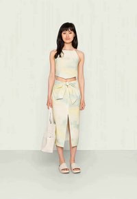 Conjunto de duas peças com um top halter curto e uma saia midi com uma abertura frontal. O tecido tem um leve padrão tie-dye em tons pastel.