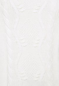 Tissu tricoté blanc avec un motif texturé de losanges, câbles et boules en relief dans un motif vertical répétitif.
