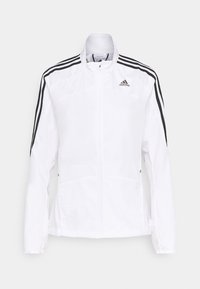 Chaqueta blanca con cremallera y logo de Adidas negro. Cuenta con rayas negras en los hombros, dos bolsillos laterales y una textura suave y ligera.