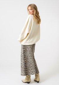 Pull crème surdimensionné assorti à une jupe midi à imprimé léopard, dotée d'un tissu lisse et d'une texture douce. Complété par des bottines à talons beiges.