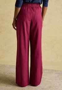 Široké nohavice s hlbokým magentovým a čiernym vertikálnym pruhovým vzorom, elastickým pásom a hladkým povrchom látky.