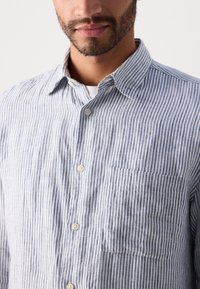 Striped button-up shirt in light blue and white. Features a collar, a chest pocket, and a linen-like texture with vertical stripes.