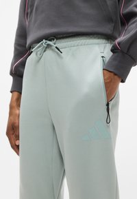 Ανοιχτό πράσινο-μέντα παντελόνι φόρμας με ελαστική μέση, κορδόνι, πλαϊνές τσέπες και διακριτικό λογότυπο Adidas στο μηρό. Ομαλή υφή.