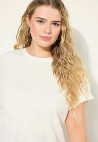 Witte katoenen t-shirt met een ronde halslijn en korte mouwen. De stof lijkt zacht met een gladde textuur en minimale ontwerpelementen.