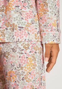 Bunte Pyjamas mit floralem Druck und hellen Hintergrund in Rosa, Orange und Braun. Weicher Stoff, lange Ärmel und gesäumte Bündchen.