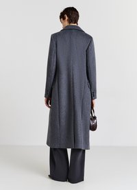 Cappotto grigio di lana con un design lungo, rever ampi e tasche laterali. Abbinato a pantaloni scuri e una piccola borsa marrone.