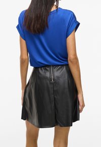 Haut bleu à manches courtes associé à une mini-jupe en cuir noir avec une fermeture éclair visible au dos et une texture lisse.