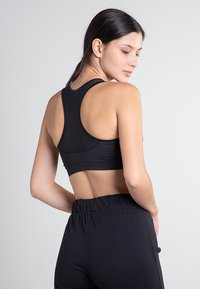 Svart sportbh med racerback-design, tillverkad av texturerad tyg med en slät yta, ihop med högmidjade svarta byxor.