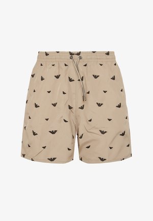 Beige swim shorts with black eagle logos printed all over, featuring an elastic waistband and drawstring closure at the front.